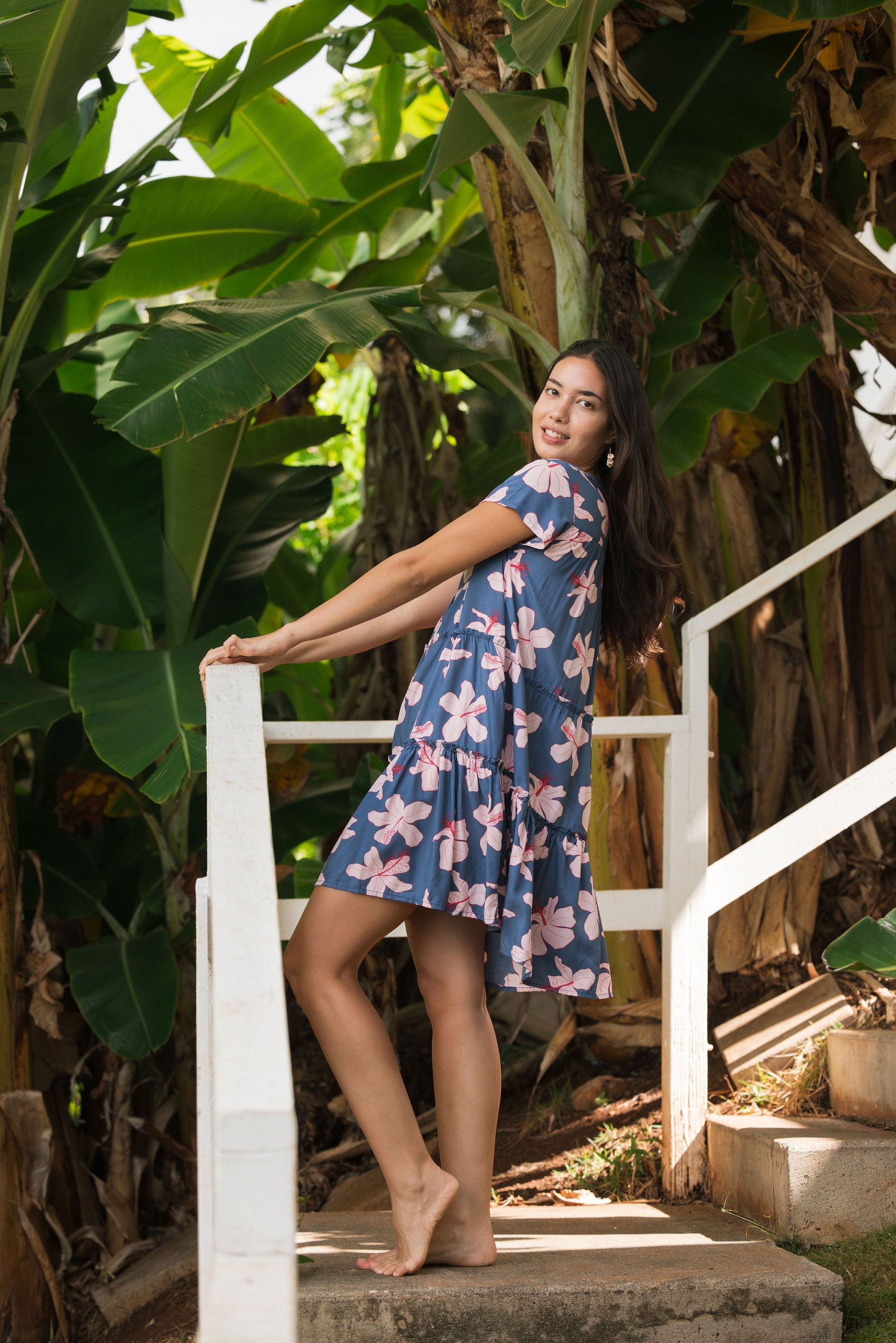 woman with black hair wearing a mini tiered dress in a navy color with pink hibiscus blossoms 