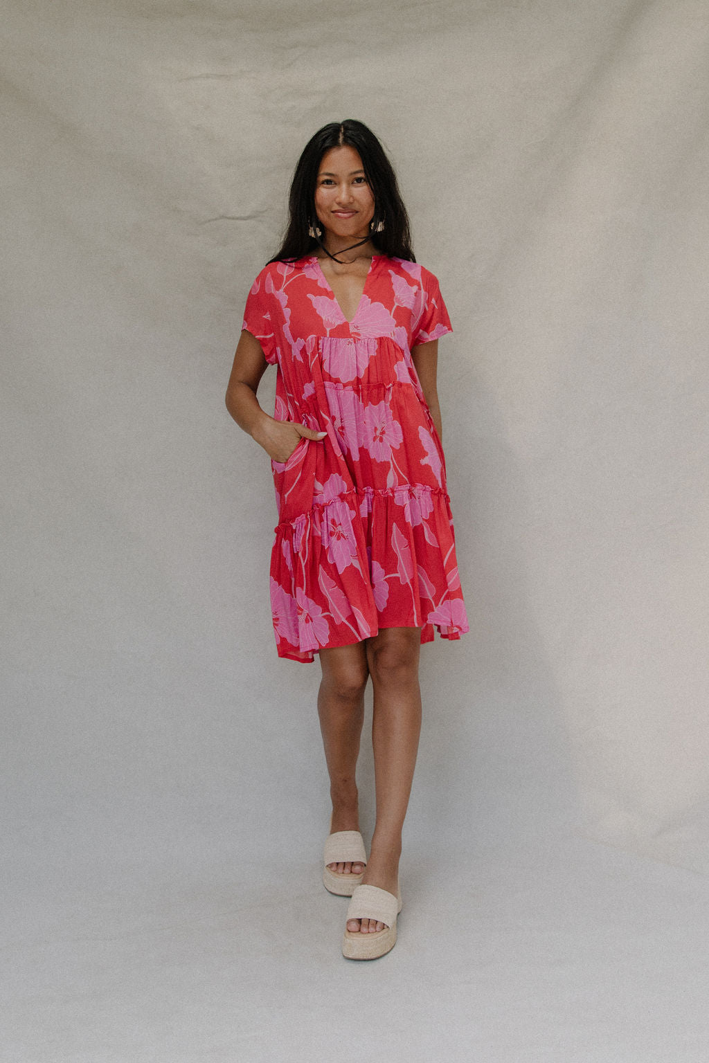 woman with brown hair wearing a red and pink v neck flowy knee length dress with mao flower pattern