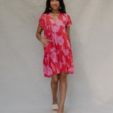 woman with brown hair wearing a red and pink v neck flowy knee length dress with mao flower pattern