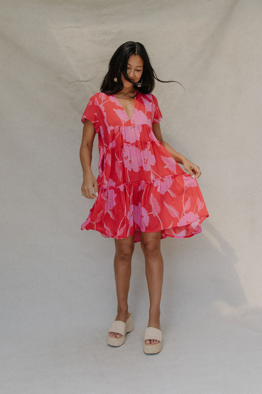 woman with brown hair wearing a red and pink v neck flowy knee length dress with mao flower pattern