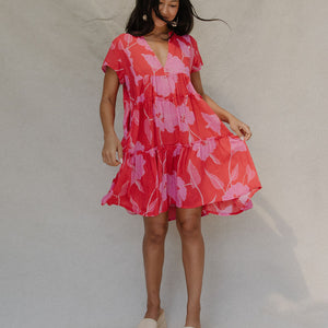 woman with brown hair wearing a red and pink v neck flowy knee length dress with mao flower pattern