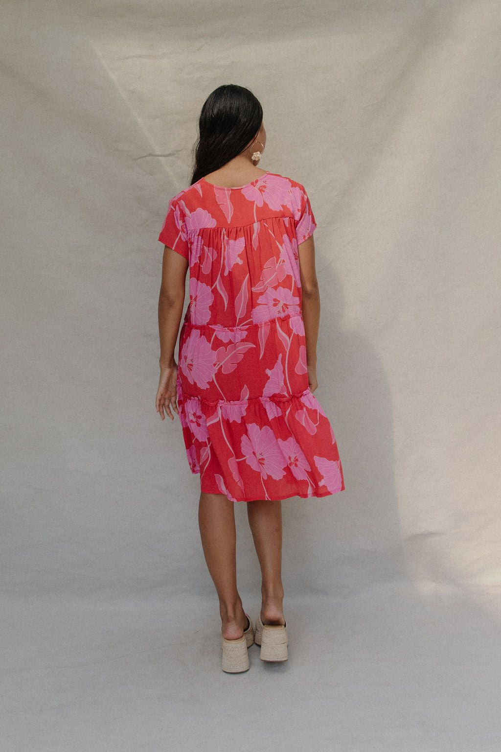 woman with brown hair wearing a red and pink v neck flowy knee length dress with mao flower pattern