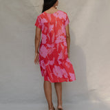 woman with brown hair wearing a red and pink v neck flowy knee length dress with mao flower pattern