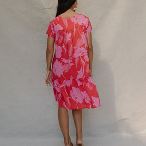 woman with brown hair wearing a red and pink v neck flowy knee length dress with mao flower pattern