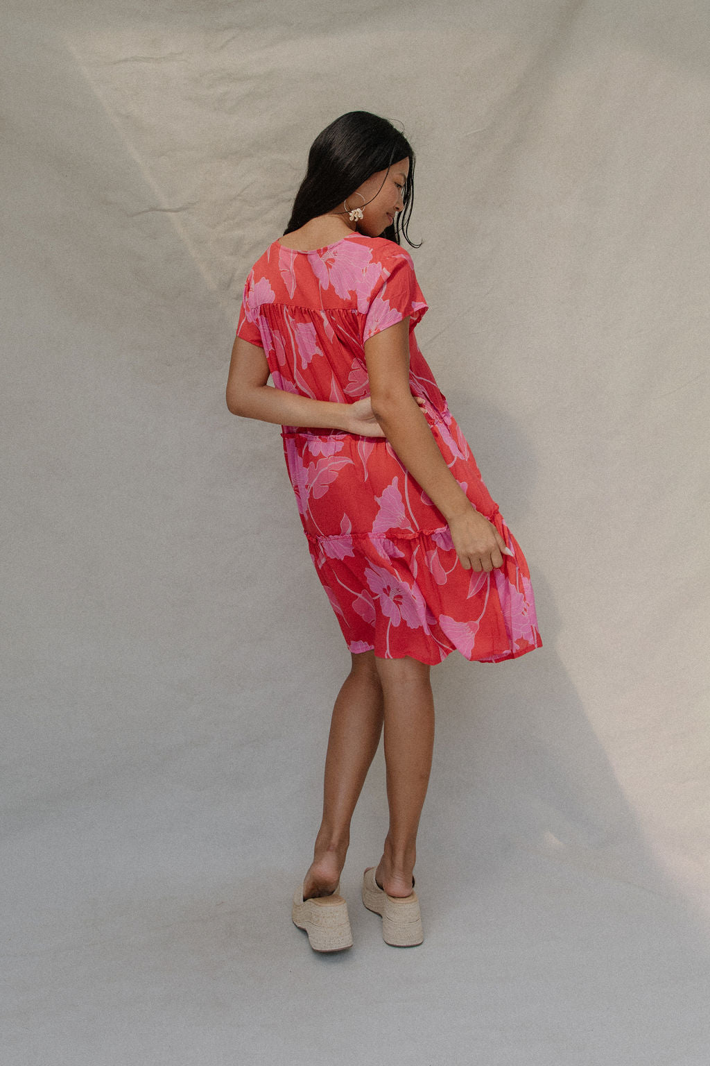 woman with brown hair wearing a red and pink v neck flowy knee length dress with mao flower pattern
