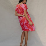 woman with brown hair wearing a red and pink v neck flowy knee length dress with mao flower pattern