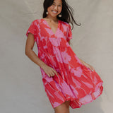 woman with brown hair wearing a red and pink v neck flowy knee length dress with mao flower pattern