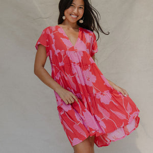 woman with brown hair wearing a red and pink v neck flowy knee length dress with mao flower pattern
