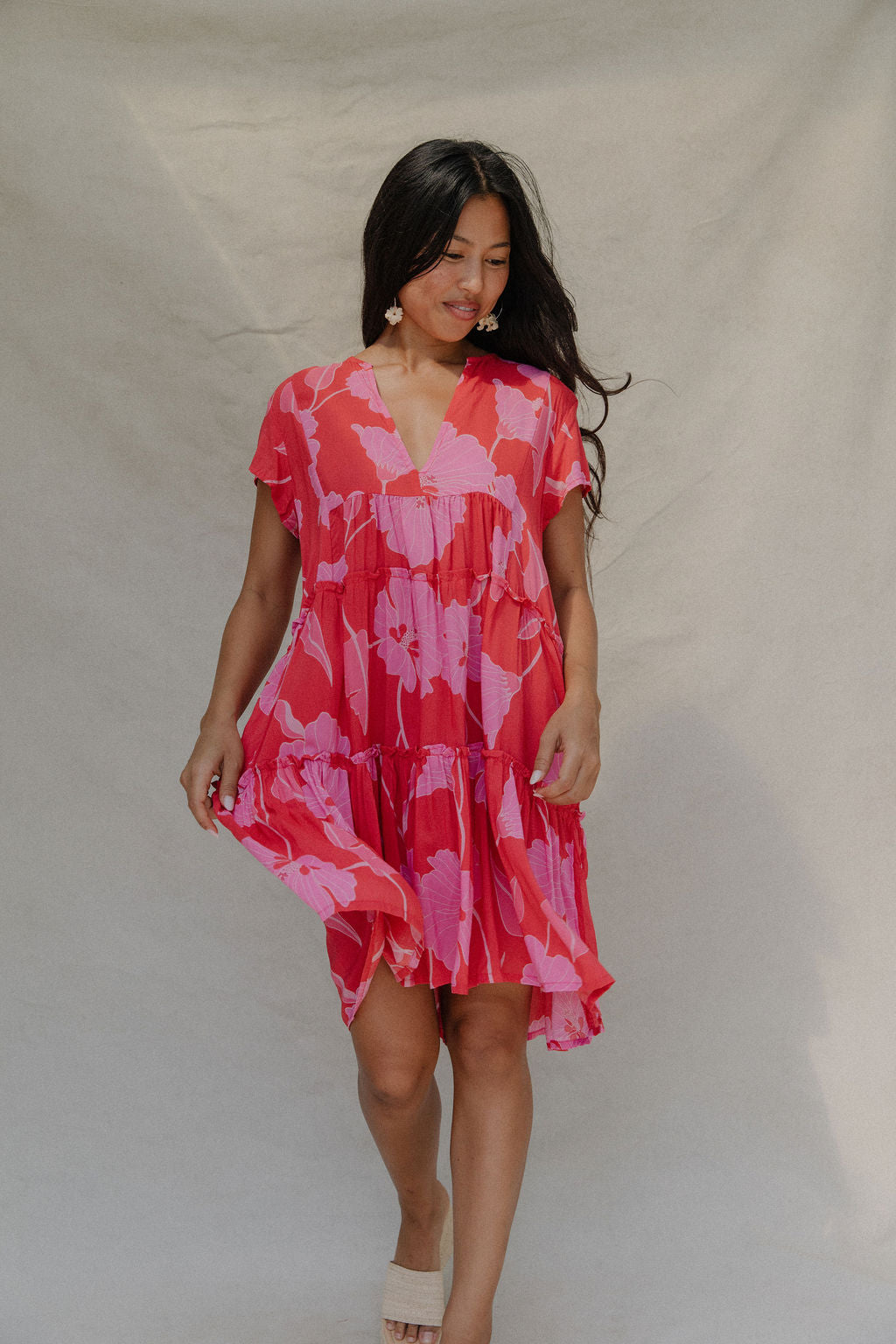 woman with brown hair wearing a red and pink v neck flowy knee length dress with mao flower pattern