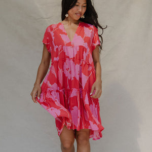 woman with brown hair wearing a red and pink v neck flowy knee length dress with mao flower pattern