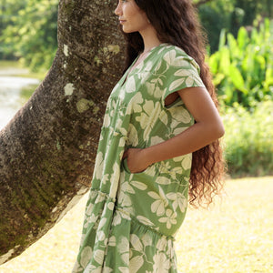 woman wearing green flowy tiered short dress with native Hawaiian plants