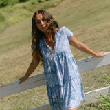 woman with brown hair wearing blue paisley printed short flowy dress with v neck