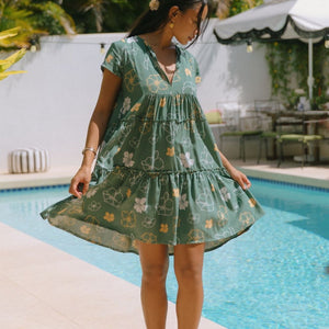 woman with brown hair wearing lush green v-neck tiered mini dress with puakenikeni print