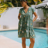 woman with brown hair wearing lush green v-neck tiered mini dress with puakenikeni print