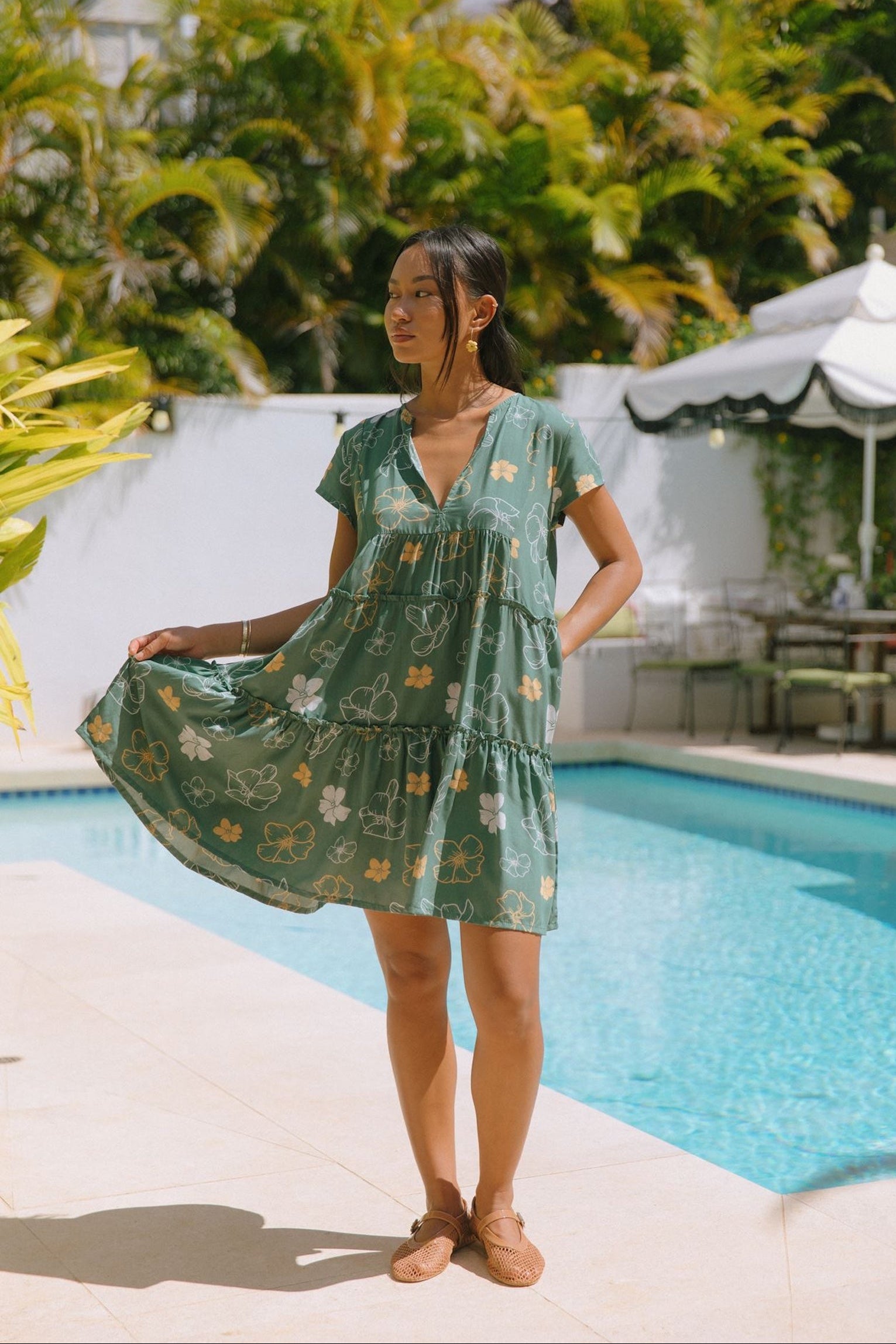 woman with brown hair wearing lush green v-neck tiered mini dress with puakenikeni print