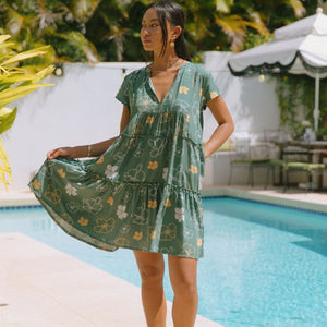 woman with brown hair wearing lush green v-neck tiered mini dress with puakenikeni print