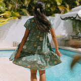 woman with brown hair wearing lush green v-neck tiered mini dress with puakenikeni print
