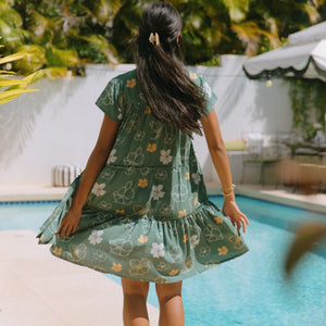 woman with brown hair wearing lush green v-neck tiered mini dress with puakenikeni print