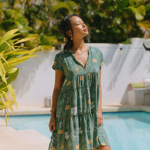 woman with brown hair wearing lush green v-neck tiered mini dress with puakenikeni print