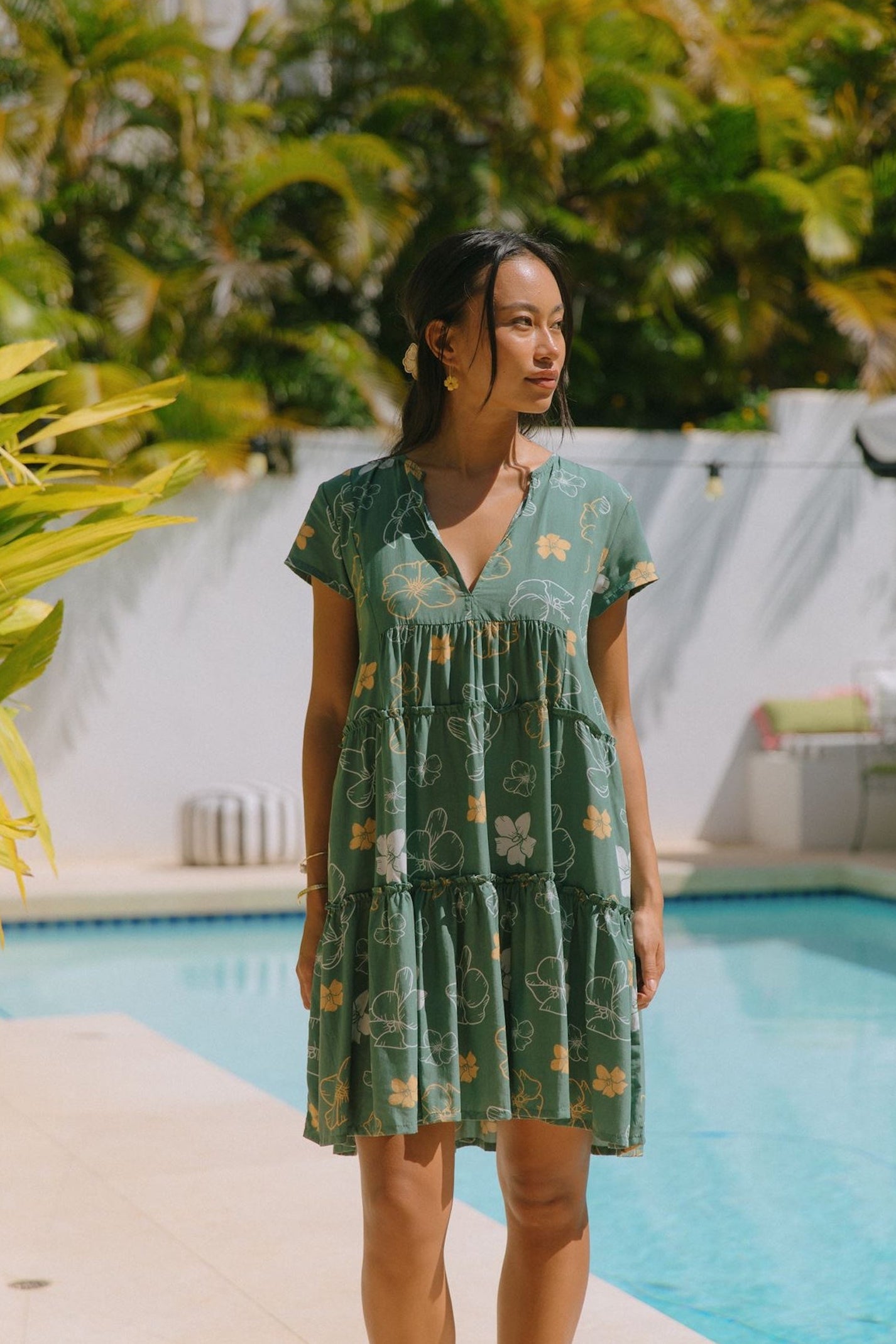 woman with brown hair wearing lush green v-neck tiered mini dress with puakenikeni print