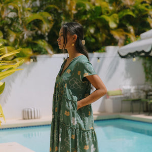 woman with brown hair wearing lush green v-neck tiered mini dress with puakenikeni print