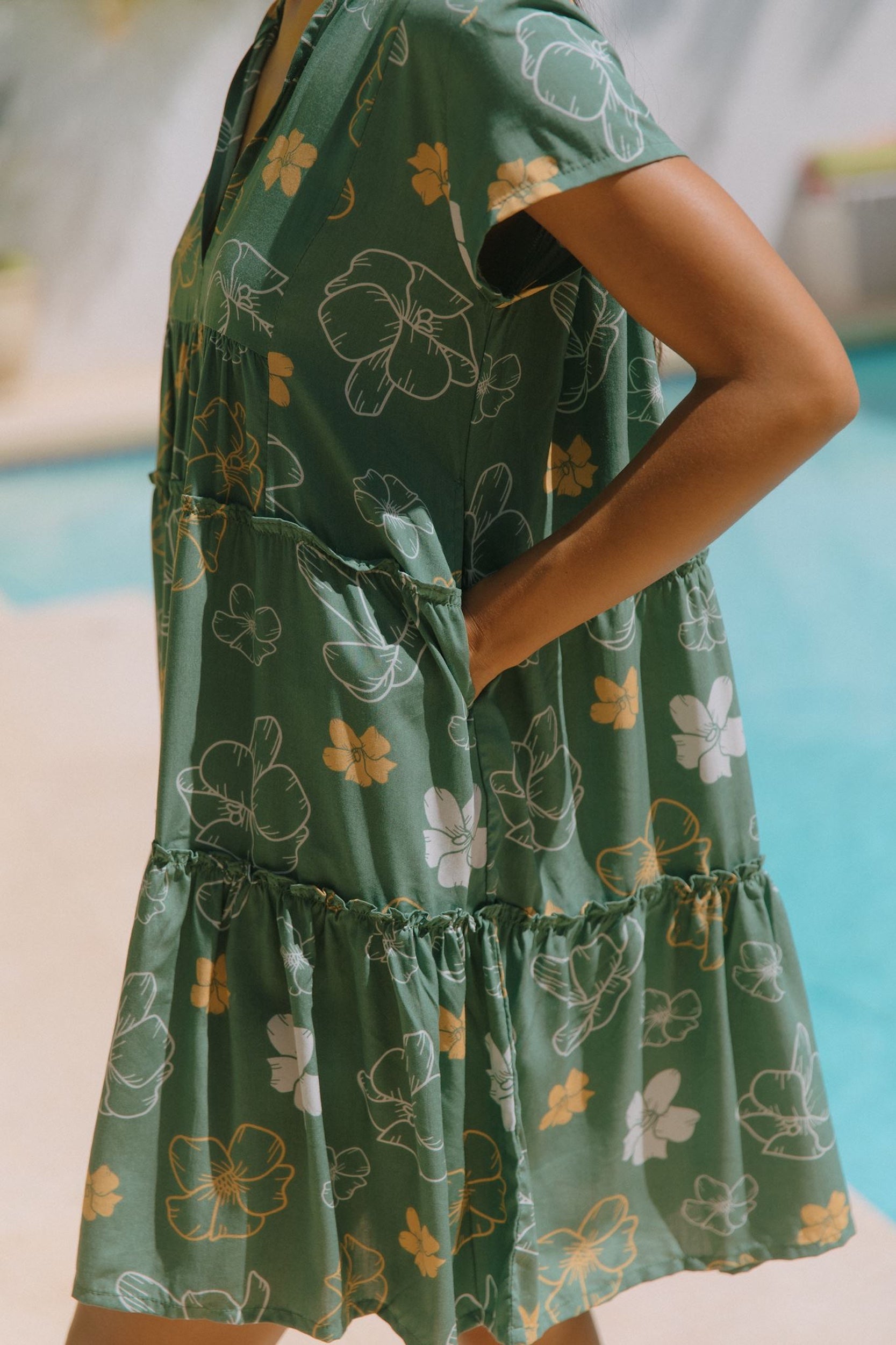 woman with brown hair wearing lush green v-neck tiered mini dress with puakenikeni print