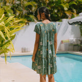 woman with brown hair wearing lush green v-neck tiered mini dress with puakenikeni print