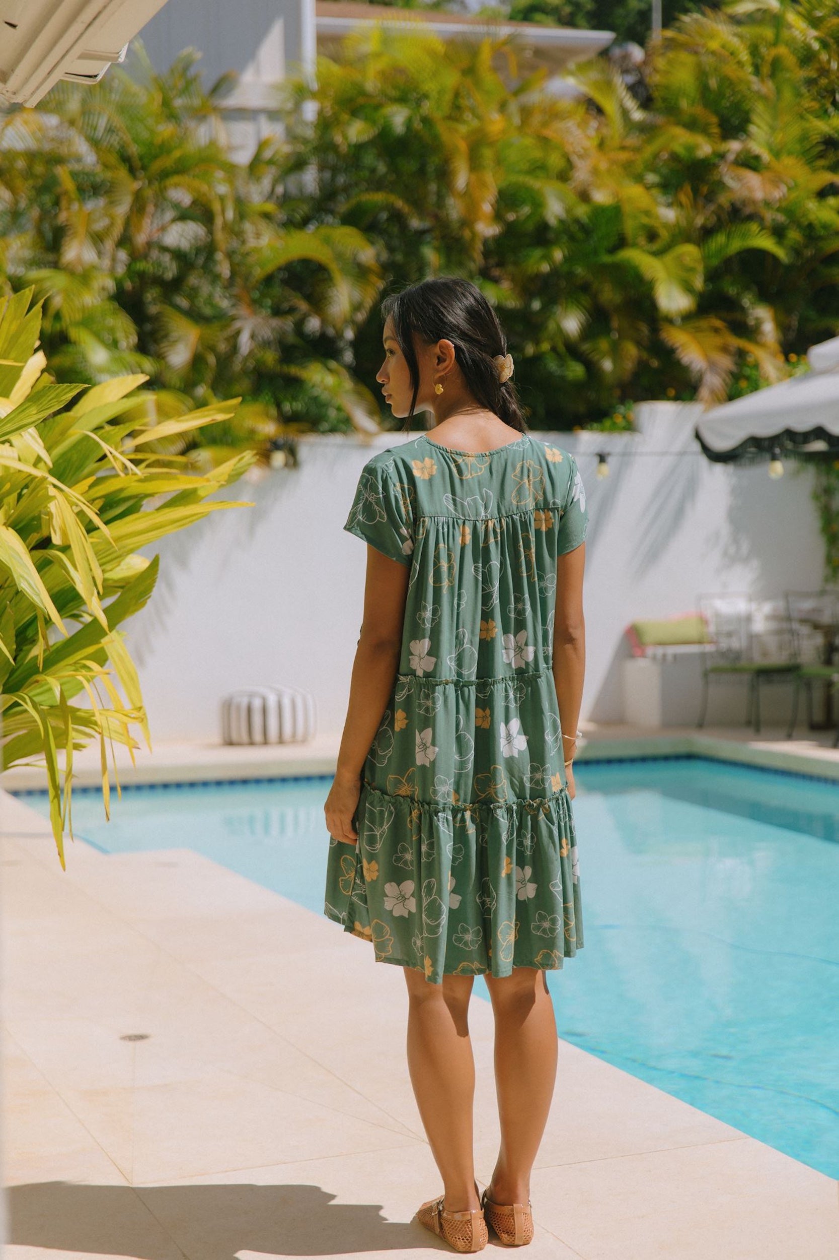 woman with brown hair wearing lush green v-neck tiered mini dress with puakenikeni print