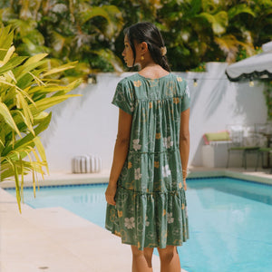 woman with brown hair wearing lush green v-neck tiered mini dress with puakenikeni print