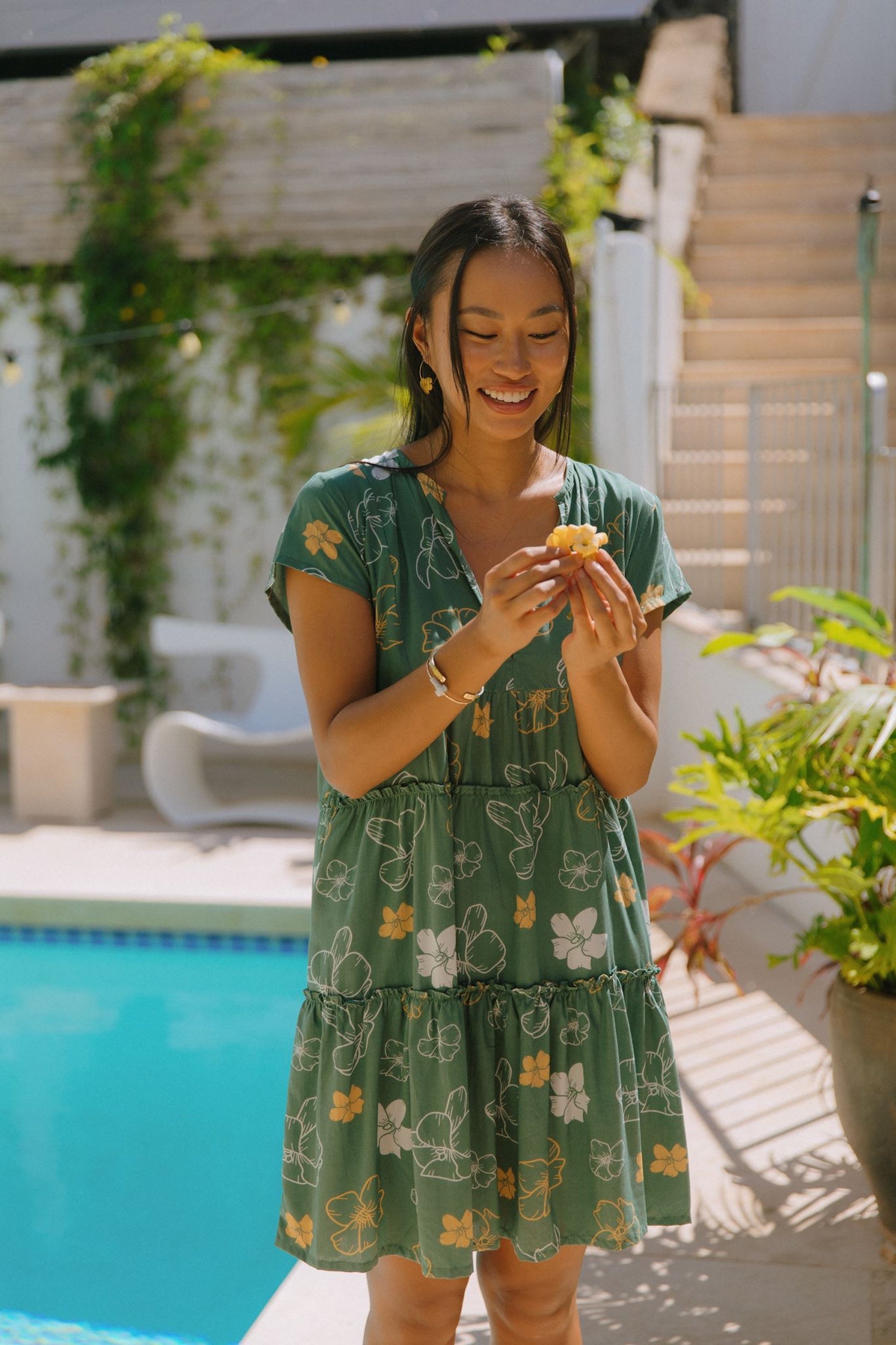 woman with brown hair wearing lush green v-neck tiered mini dress with puakenikeni print