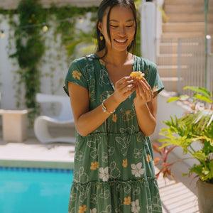 woman with brown hair wearing lush green v-neck tiered mini dress with puakenikeni print