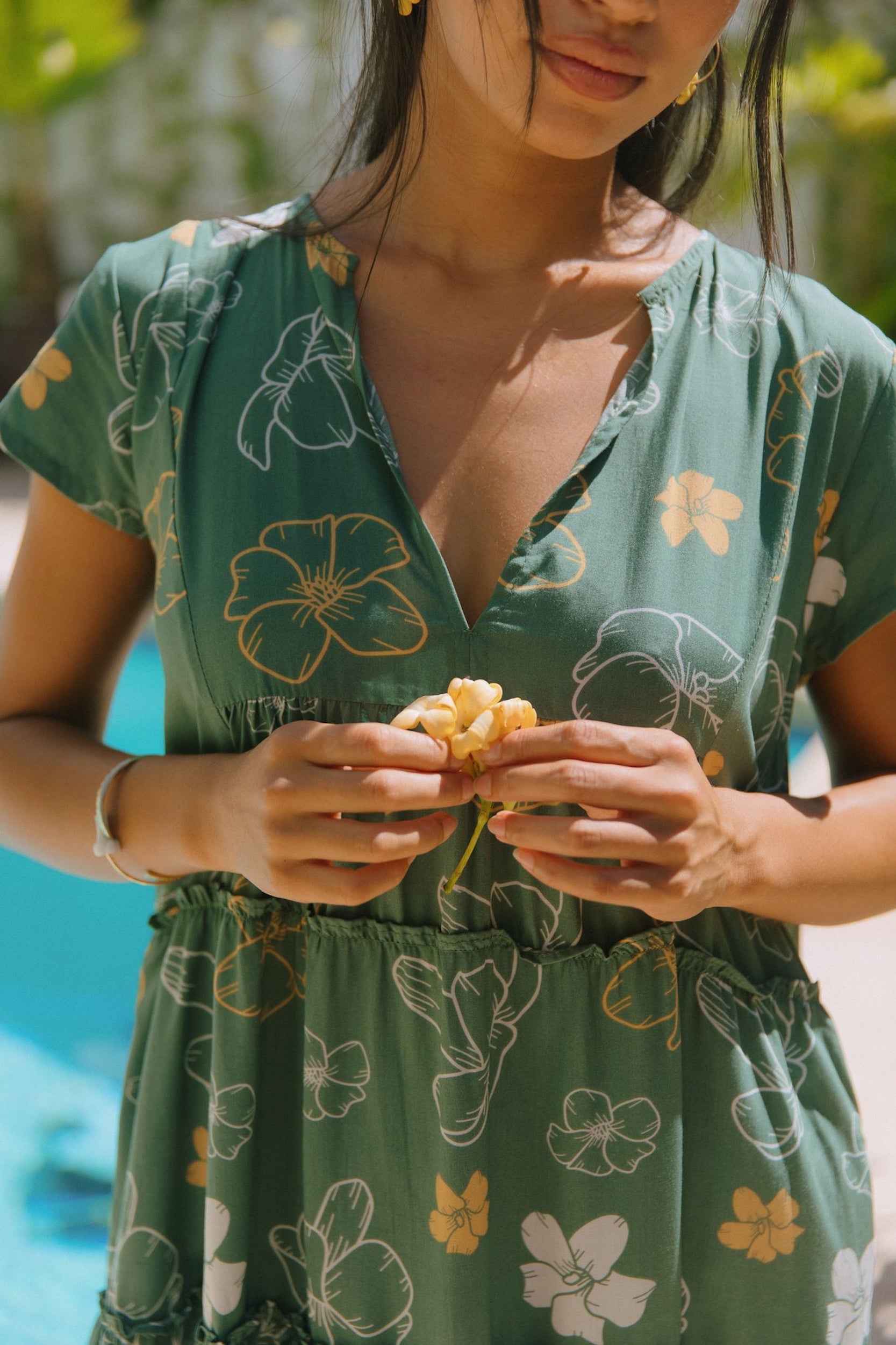 woman with brown hair wearing lush green v-neck tiered mini dress with puakenikeni print