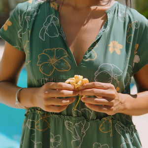 woman with brown hair wearing lush green v-neck tiered mini dress with puakenikeni print