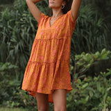 woman with brown hair wearing an orange v neck flowy over sized dress with puakenikeni print