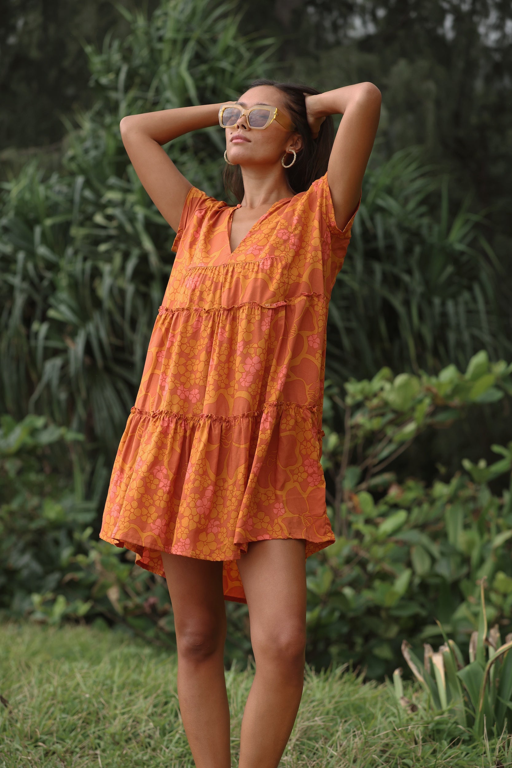 woman with brown hair wearing an orange v neck flowy over sized dress with puakenikeni print