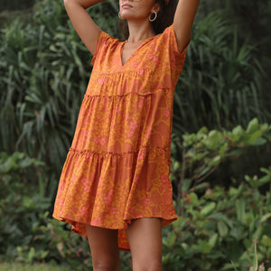 woman with brown hair wearing an orange v neck flowy over sized dress with puakenikeni print