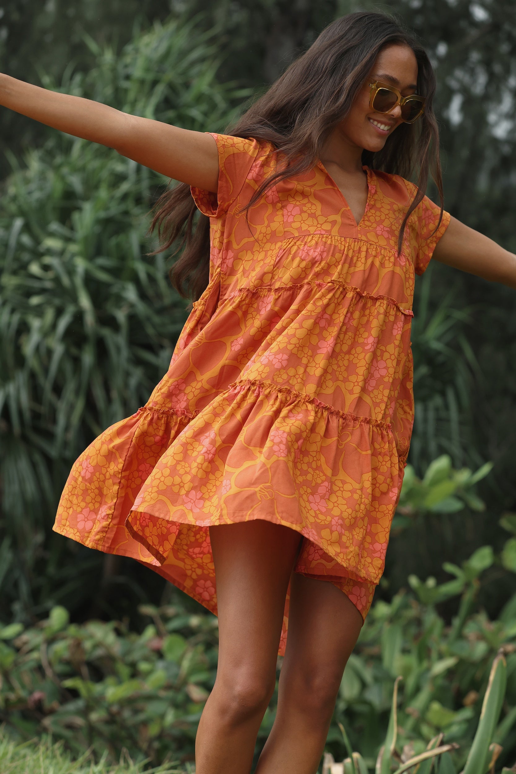 woman with brown hair wearing an orange v neck flowy over sized dress with puakenikeni print