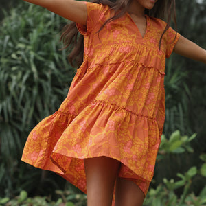 woman with brown hair wearing an orange v neck flowy over sized dress with puakenikeni print