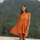woman with brown hair wearing an orange v neck flowy over sized dress with puakenikeni print