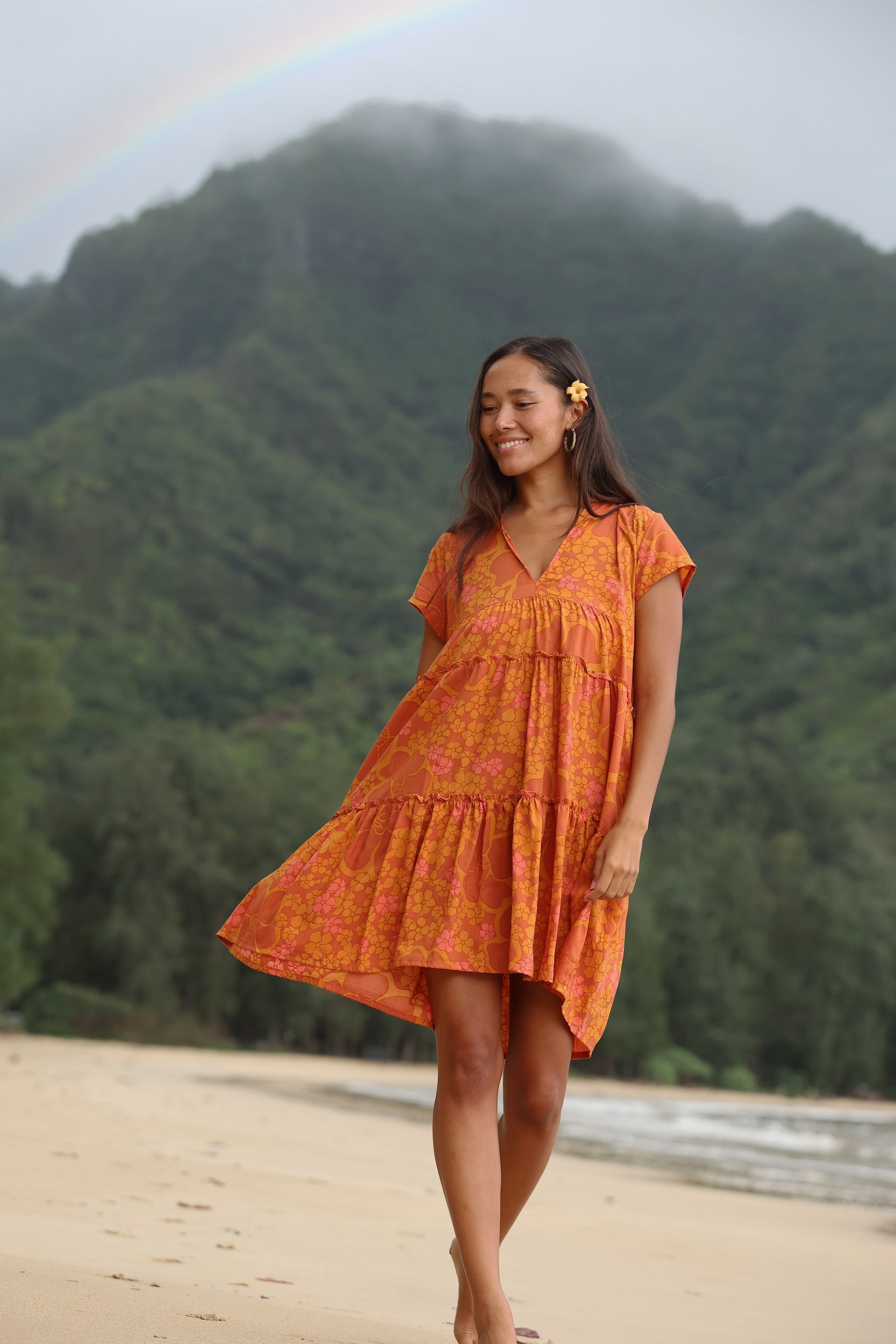 woman with brown hair wearing an orange v neck flowy over sized dress with puakenikeni print