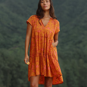 woman with brown hair wearing an orange v neck flowy over sized dress with puakenikeni print