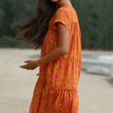 woman with brown hair wearing an orange v neck flowy over sized dress with puakenikeni print