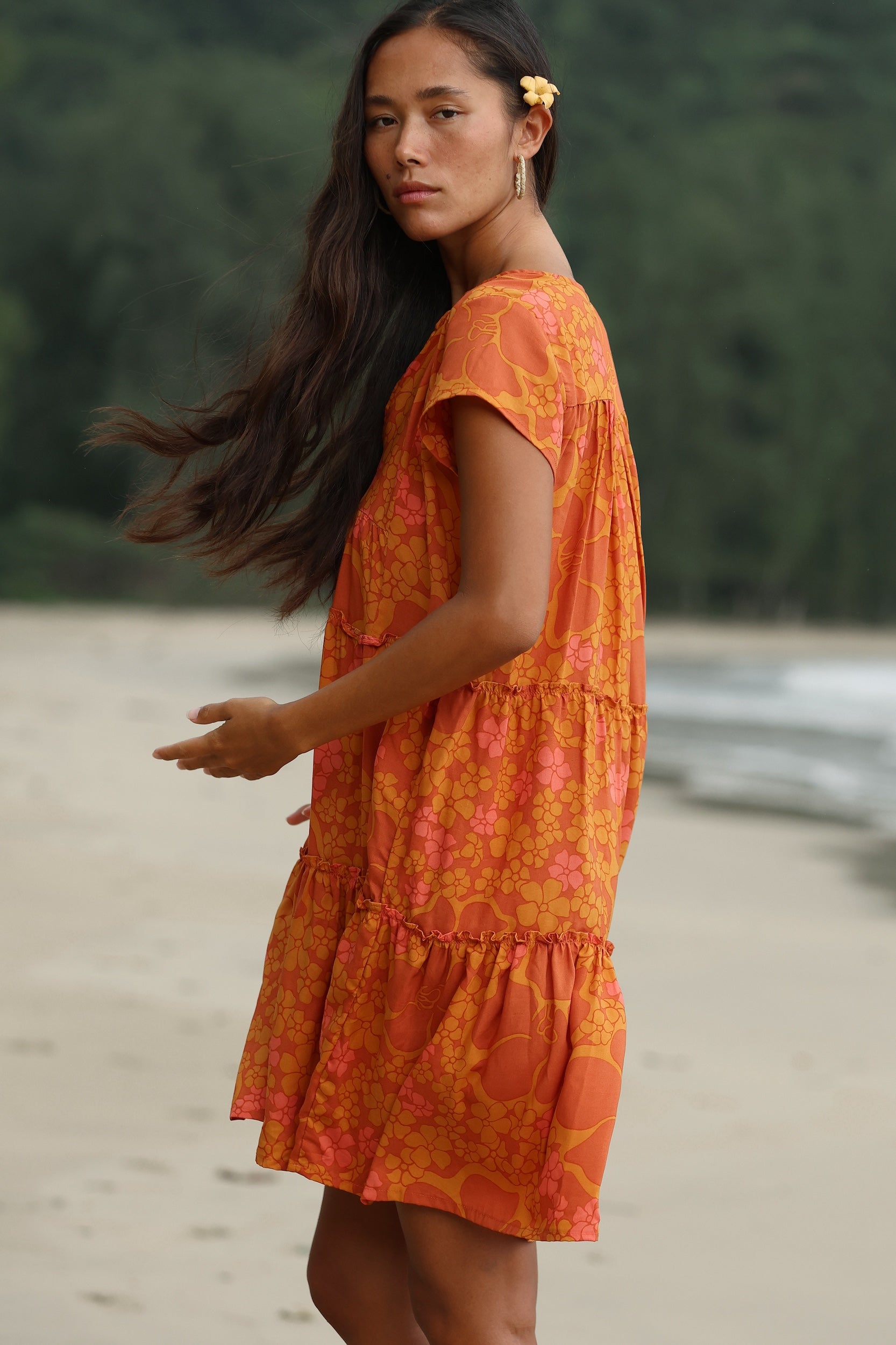 woman with brown hair wearing an orange v neck flowy over sized dress with puakenikeni print