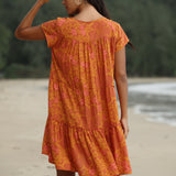 woman with brown hair wearing an orange v neck flowy over sized dress with puakenikeni print