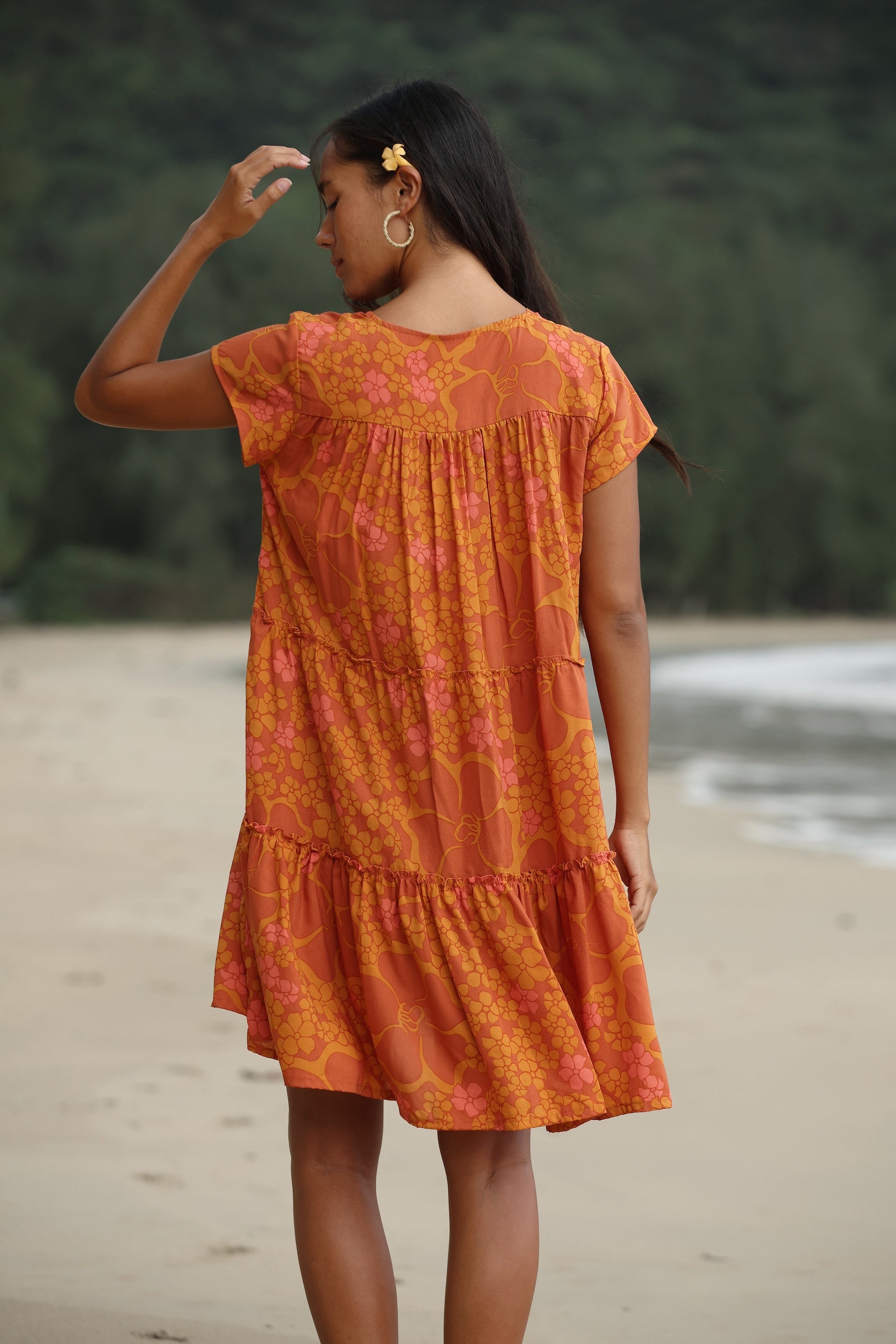 woman with brown hair wearing an orange v neck flowy over sized dress with puakenikeni print