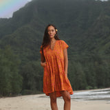 woman with brown hair wearing an orange v neck flowy over sized dress with puakenikeni print