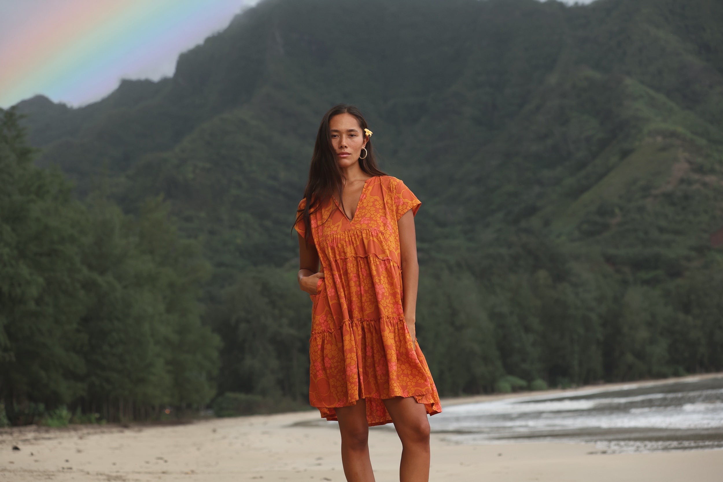 woman with brown hair wearing an orange v neck flowy over sized dress with puakenikeni print