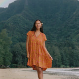 woman with brown hair wearing an orange v neck flowy over sized dress with puakenikeni print
