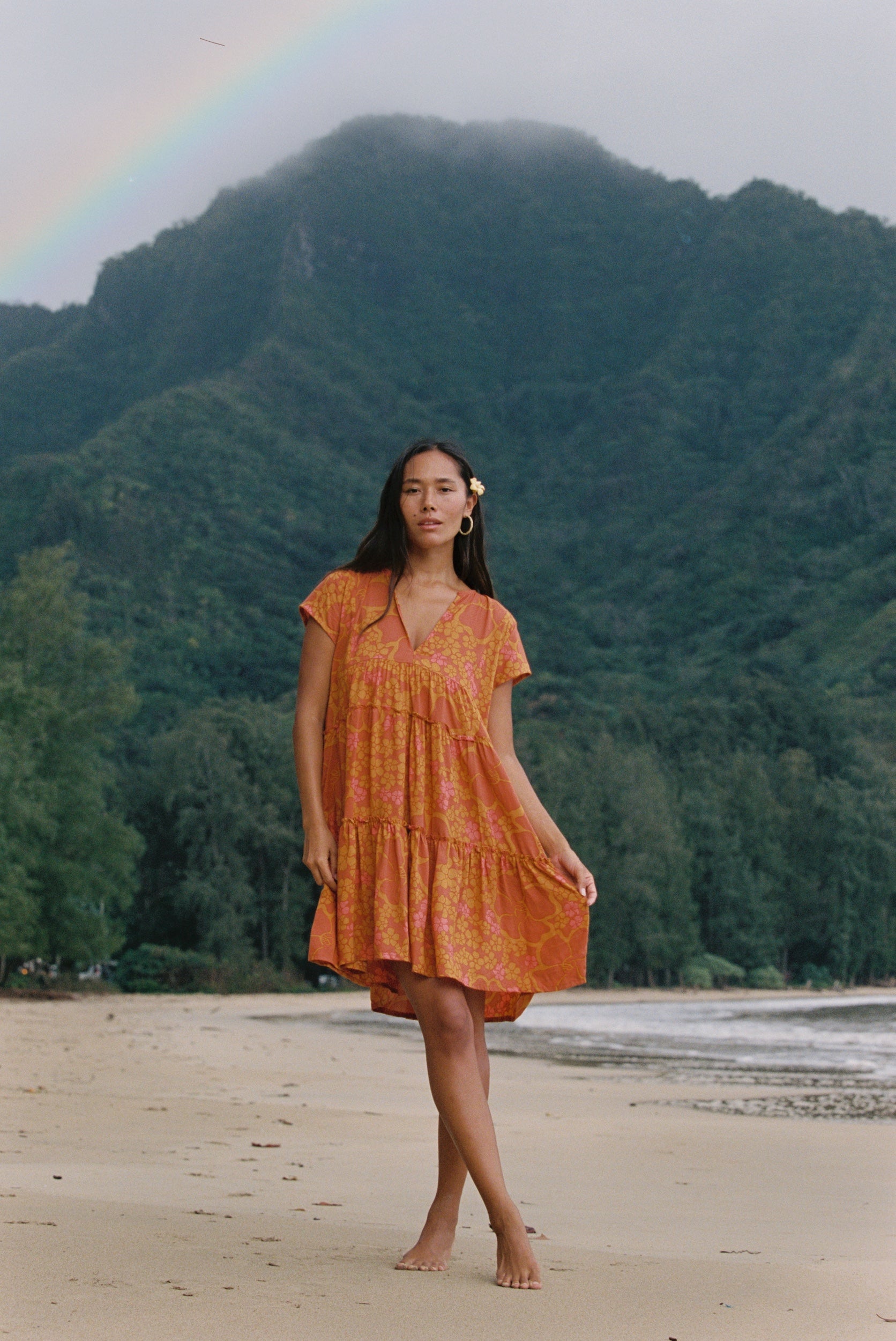 woman with brown hair wearing an orange v neck flowy over sized dress with puakenikeni print