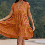 woman with brown hair wearing an orange v neck flowy over sized dress with puakenikeni print
